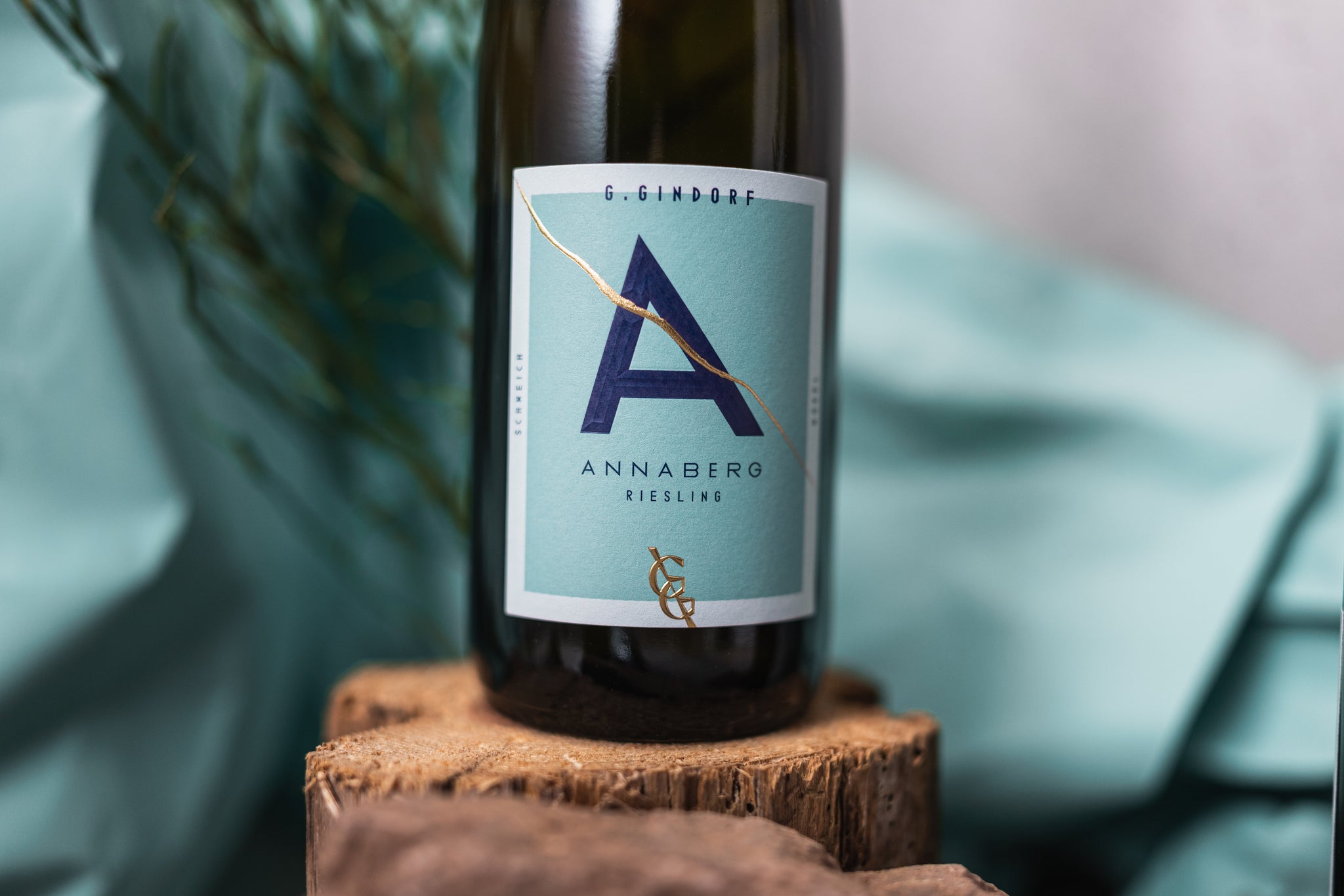 Flasche Annaberg Riesling vom Weingut Gindorf auf einem Holzstück, stilvoll fotografiert vor türkisfarbenem Hintergrund.