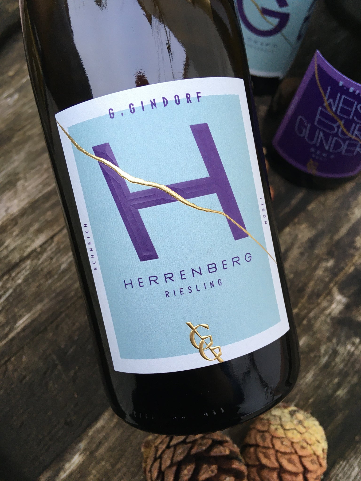 Nahaufnahme einer G. Gindorf-Herrenberg Rieslingflasche mit modernem türkis-violettem Etikett auf rustikalem Holztisch.