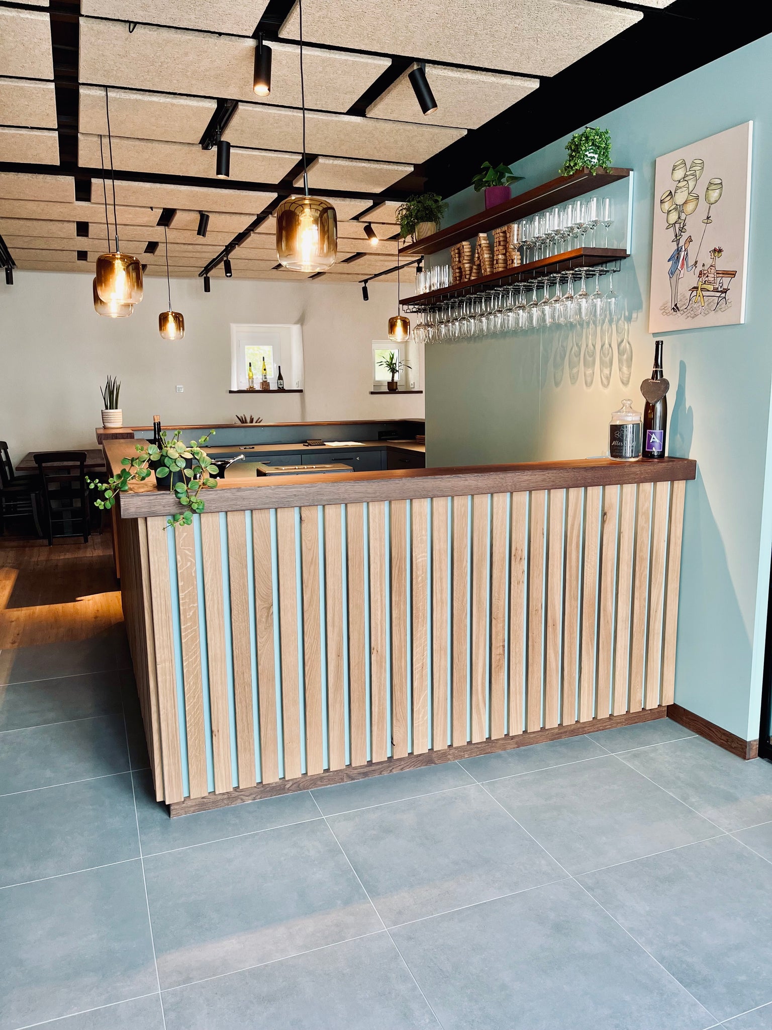 Moderne Weinbar des Weinguts Günter Gindorf in Schweich mit stilvoller Holztheke, hängenden Weingläsern, warmen Pendelleuchten und hellblauer Wandgestaltung – einladendes Ambiente für Weinproben an der Mosel.