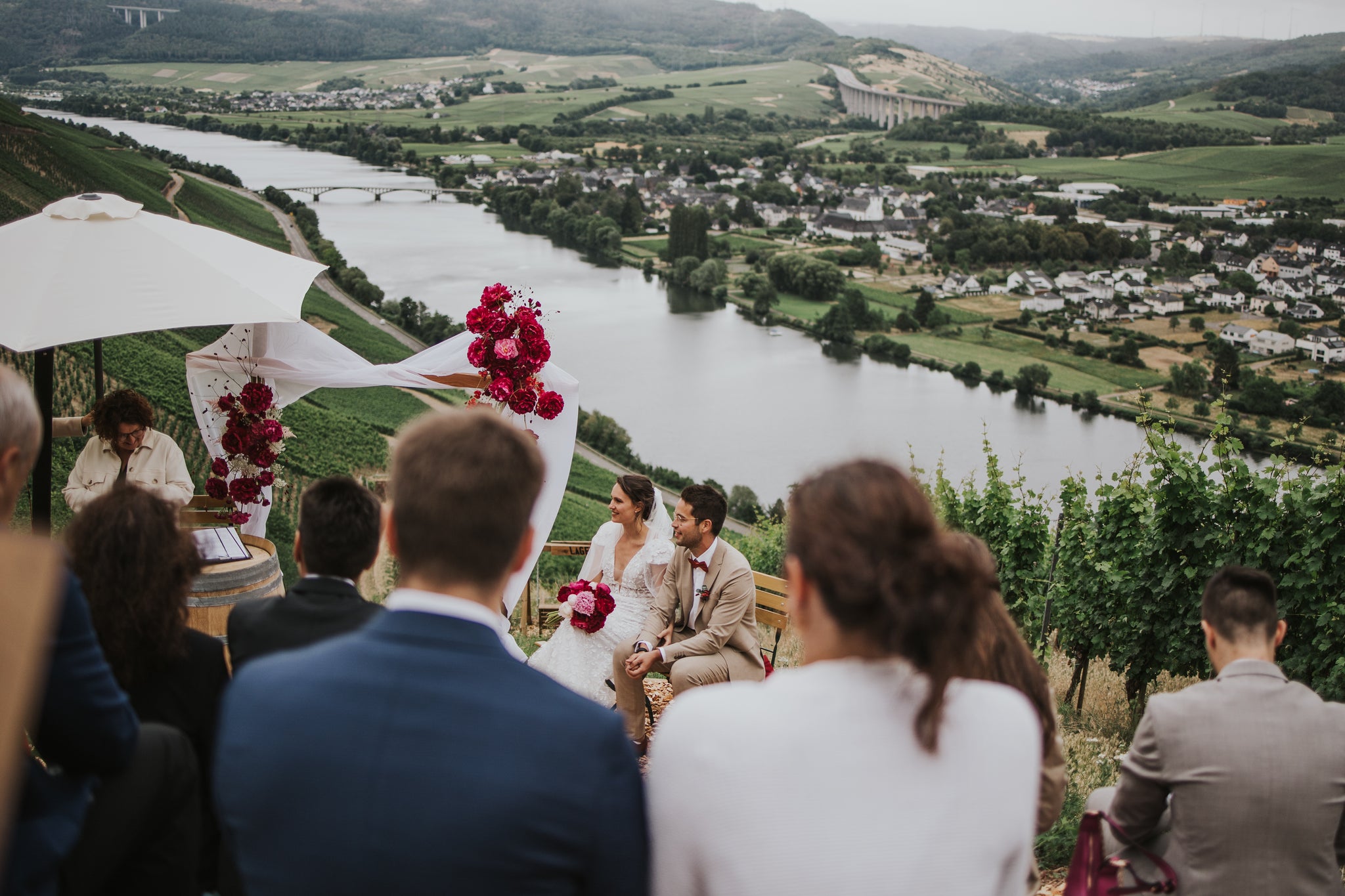 Freie Trauung in den Weinbergen oberhalb von Schweich mit Blick auf die Mosel – Hochzeitszeremonie zwischen Reben, dekoriert mit roten Blumen und Panoramablick über das Moseltal.